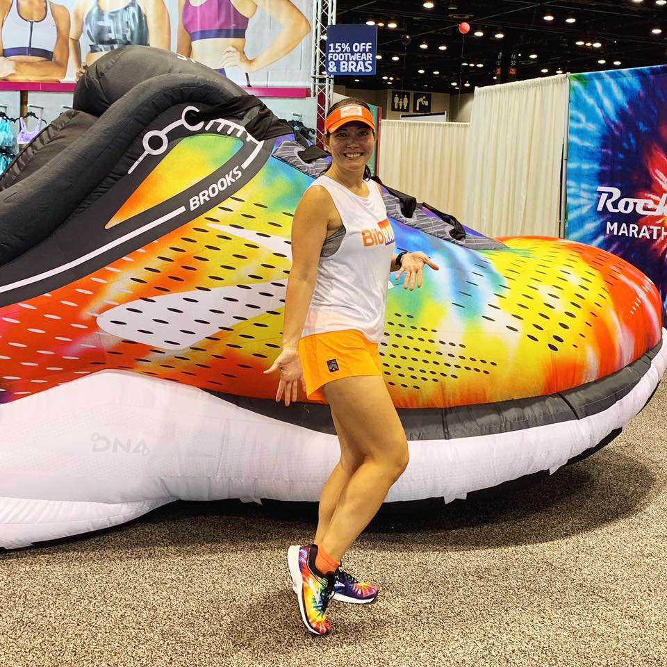 Standing in front of an inflatable Brooks Launch shoe while wearing my new, matching rainbow tie-dyed shoes.