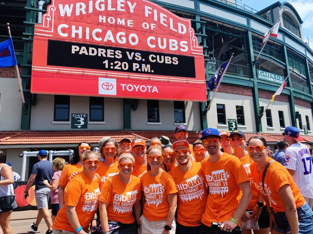 BibRave team wearing all orange in front of the Wrigley Field sign.