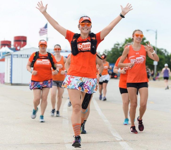 Running with the BibRave team in all orange with my arms outstretched in victory.