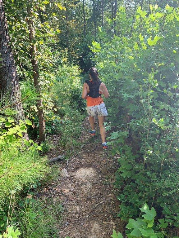 Running on a tree root covered single track trail through some thick shrubbery.