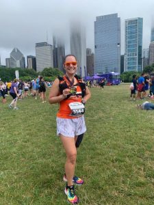 Standing at the Rock N Roll Chicago finishers festival showing my half marathon medal with the Chicago city skyline in the background.