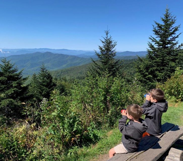 The boys sitting on a bench and testing their new binoculars looking over the mountainside.