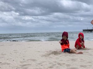 The boys playing in the sand at the beach. Wearing bright red coats and bundled up as it was pretty windy.